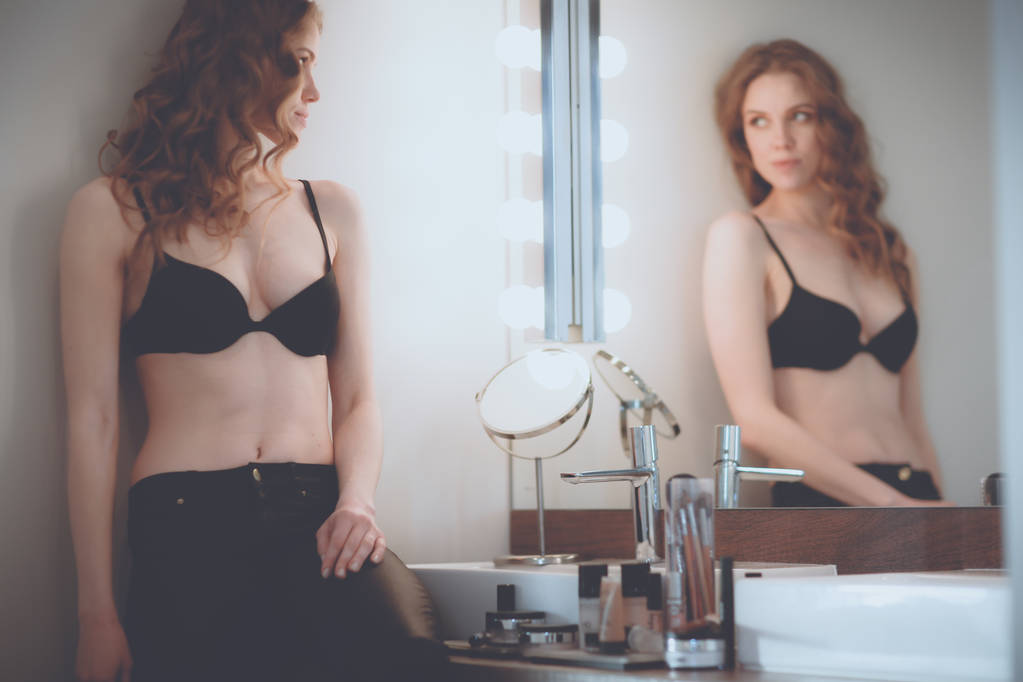 Jonge vrouw zoekt zichzelf in de spiegel op de badkamer - Foto, afbeelding