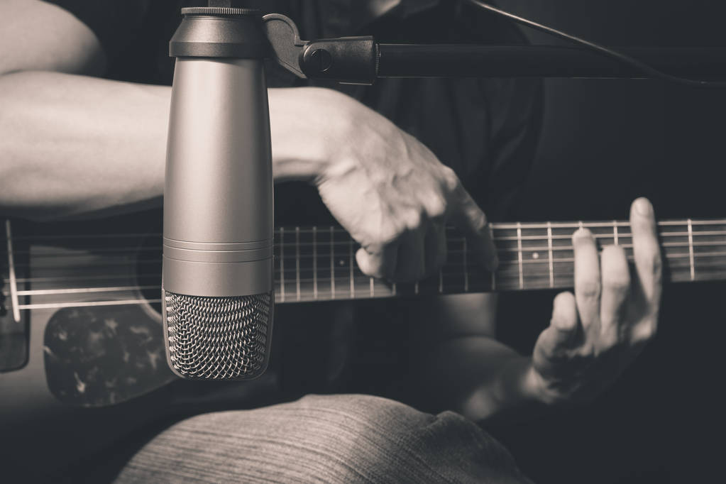 männlicher Musiker spielt Akustikgitarre hinter Kondensatormikrofon im Tonstudio - Foto, Bild