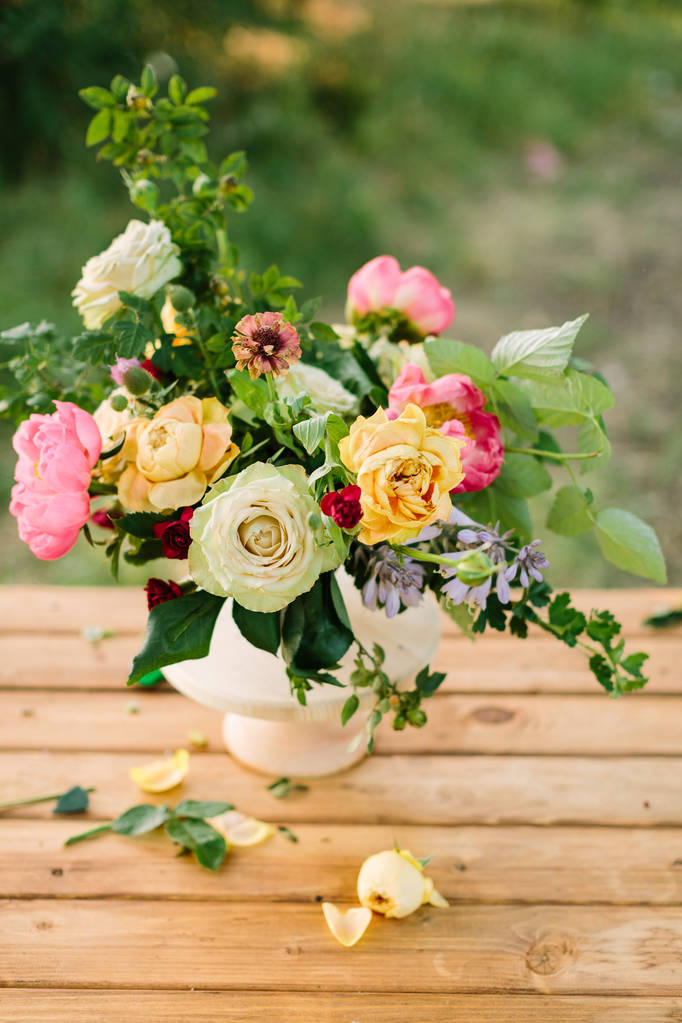 花束、祝花、ギフト、フラワーアレンジメント コンセプト - 美しい黄色と白バラの花、ピンクの魅力的な未熟練労働者、カーネーション、白い花瓶を緑の背景の野生のバラ、木製テーブルの撮影. - 写真・画像