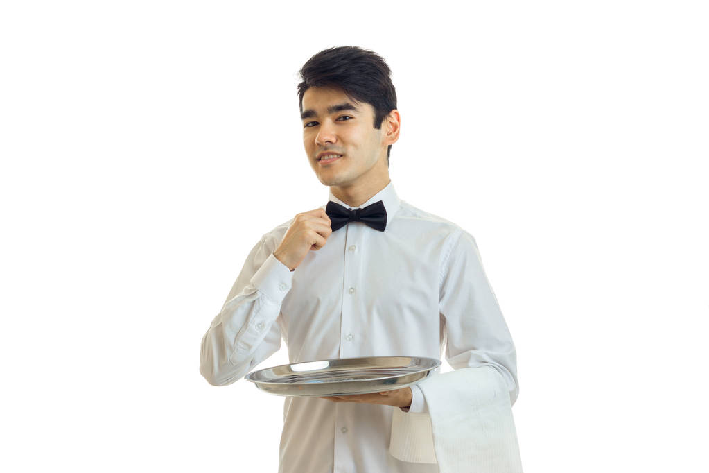 Очаровательный официант в белой рубашке держит поднос, и регулирует свой лук
 - Фото, изображение