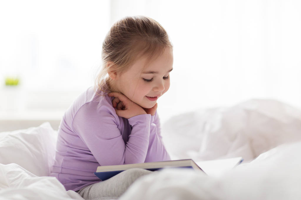 glückliches kleines Mädchen liest Buch zu Hause im Bett - Foto, Bild