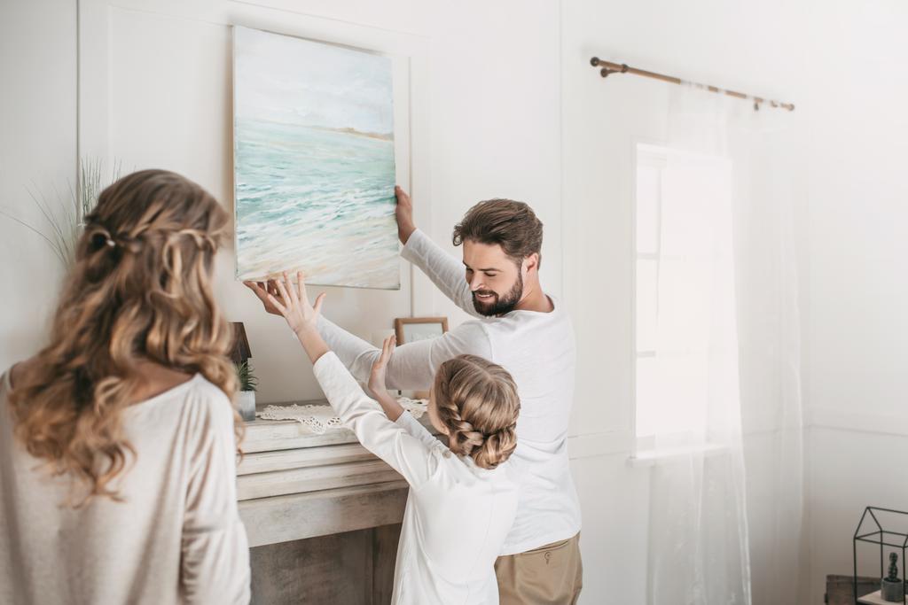 Happy family hanging picture of sea over the fireplace at home - Photo, Image