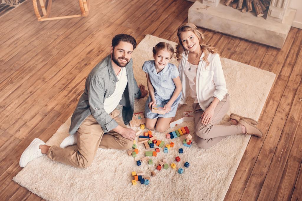 ευτυχισμένη οικογένεια παίζει με κατασκευή και κάθεται στο πάτωμα στο σπίτι - Φωτογραφία, εικόνα