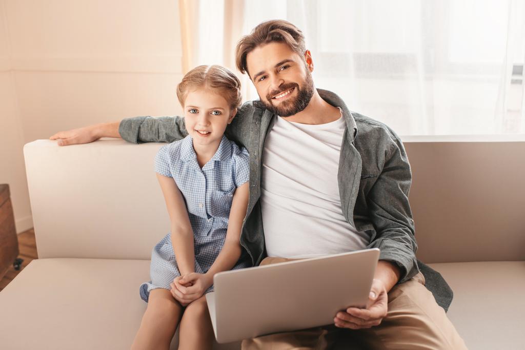 Felice padre e figlia seduti sul divano e utilizzando il computer portatile a casa
   - Foto, immagini