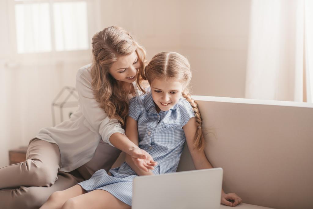 Onnellinen äiti ja tytär istuu sohvalla ja käyttää kannettavaa tietokonetta kotona
   - Valokuva, kuva