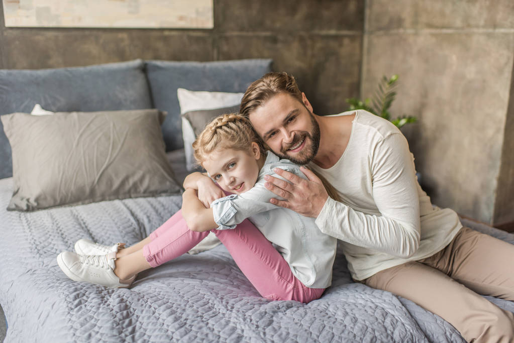 Ευτυχισμένος αξιολάτρευτη κόρη και πατέρας κάθεται στο κρεβάτι στο σπίτι - Φωτογραφία, εικόνα