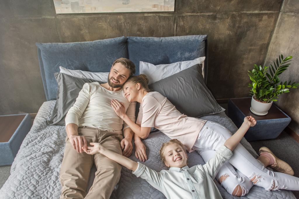 happy adorable daughter with mother and father relaxing on bed at home - Photo, Image