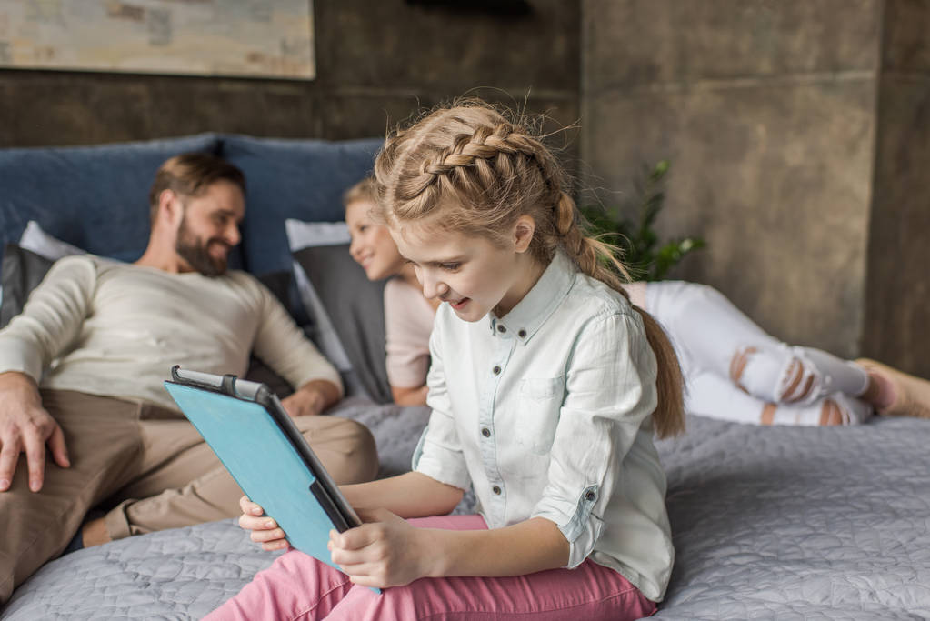 чарівна дочка використовує цифровий планшет і лежить на ліжку з батьками
 - Фото, зображення