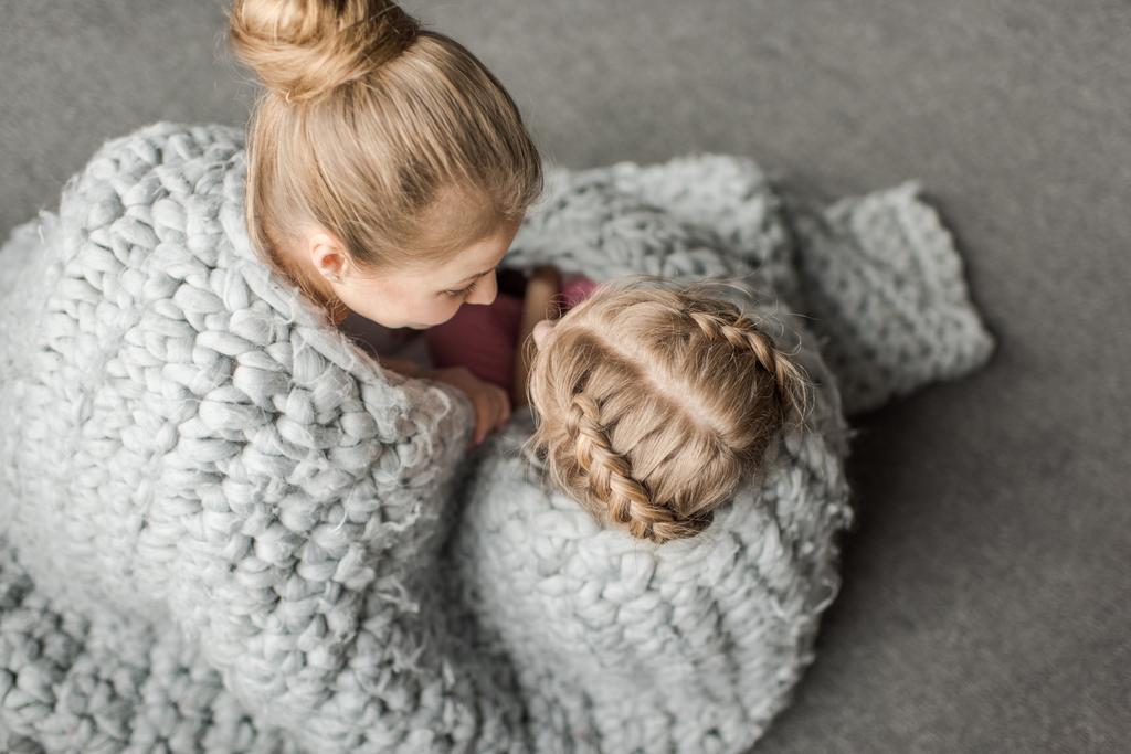 anya és lánya, átölelve hoznak, és ül a földön kötött gyapjú takaró a felülnézeti - Fotó, kép