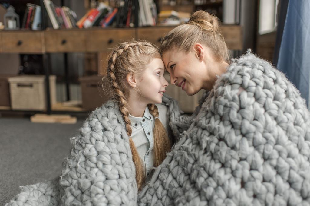 Beautiful happy mother and daughter sitting together under merino wool blanket - Photo, Image