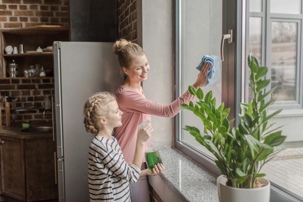 Счастливая мать и дочь моют окно тряпкой и баллончиком вместе
 - Фото, изображение