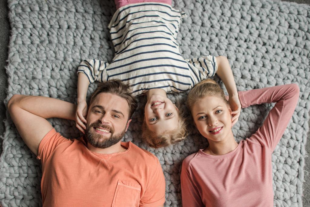Pohled shora šťastná rodina s jedním dítětem, které leží vedle sebe na šedé pletené koberec - Fotografie, Obrázek