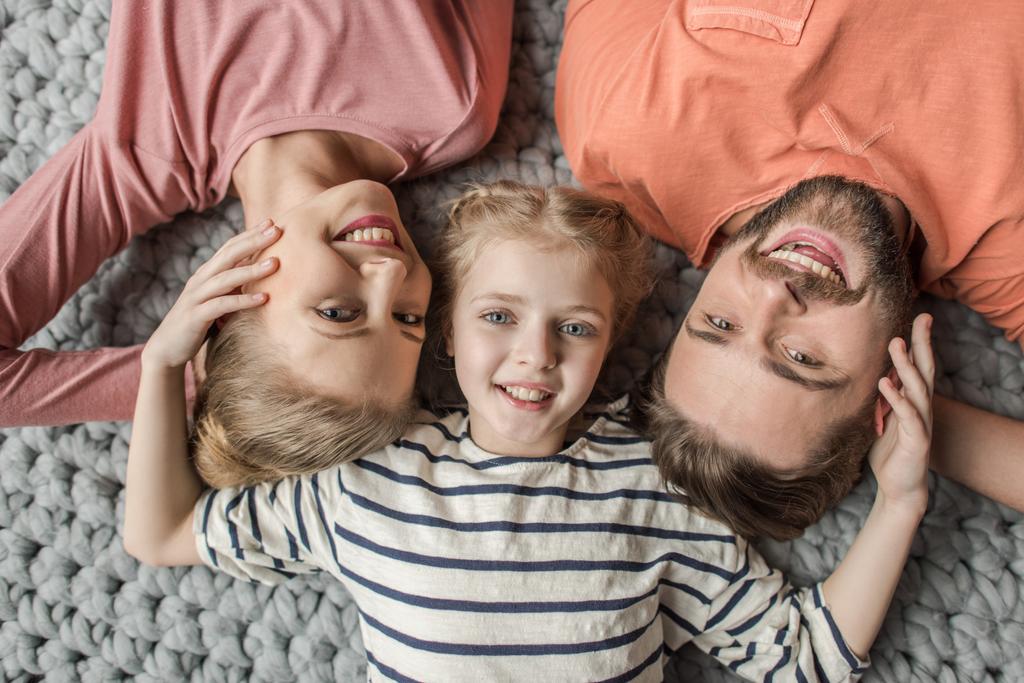 Draufsicht auf glückliche Familie mit einem Kind, das zusammen auf grauem Strickteppich liegt - Foto, Bild