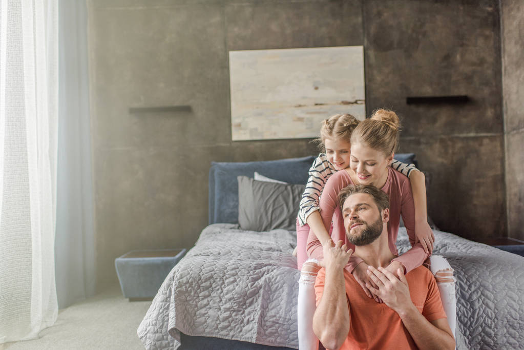 glückliche junge Familie mit einem Kind, das zusammen sitzt und sich im Schlafzimmer umarmt - Foto, Bild