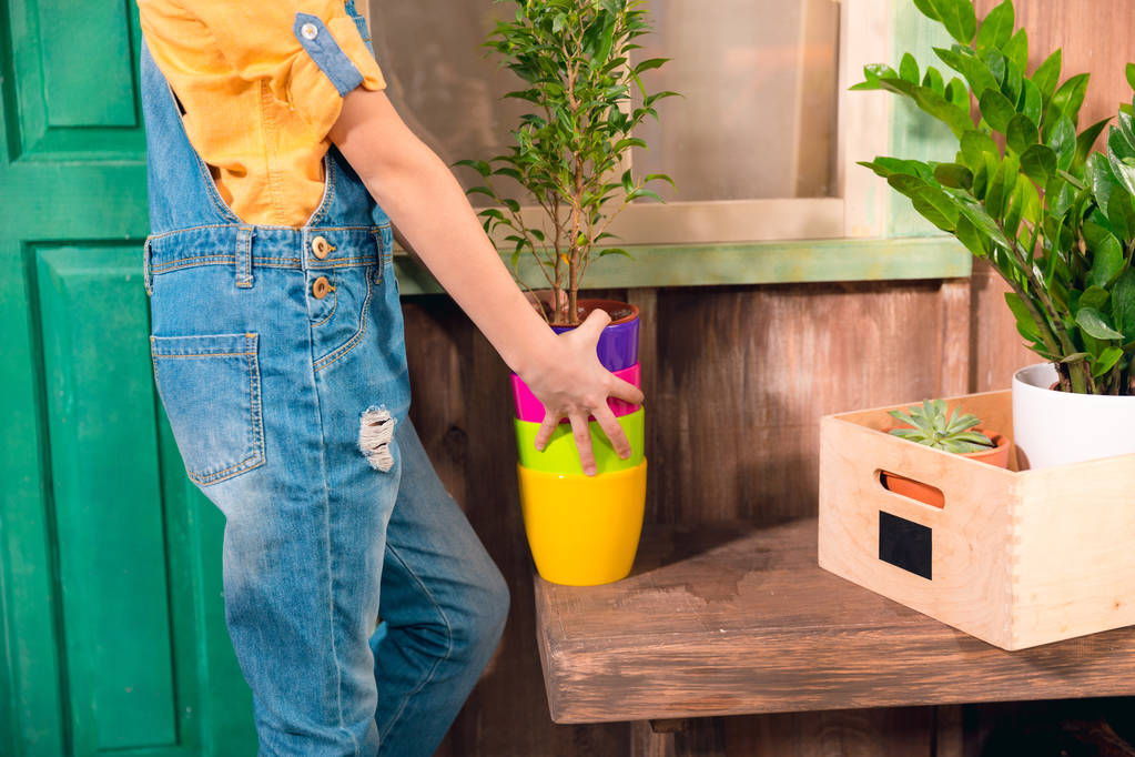 Close-up partial view of girl in dungarees holding colorful pots on porch - Photo, Image