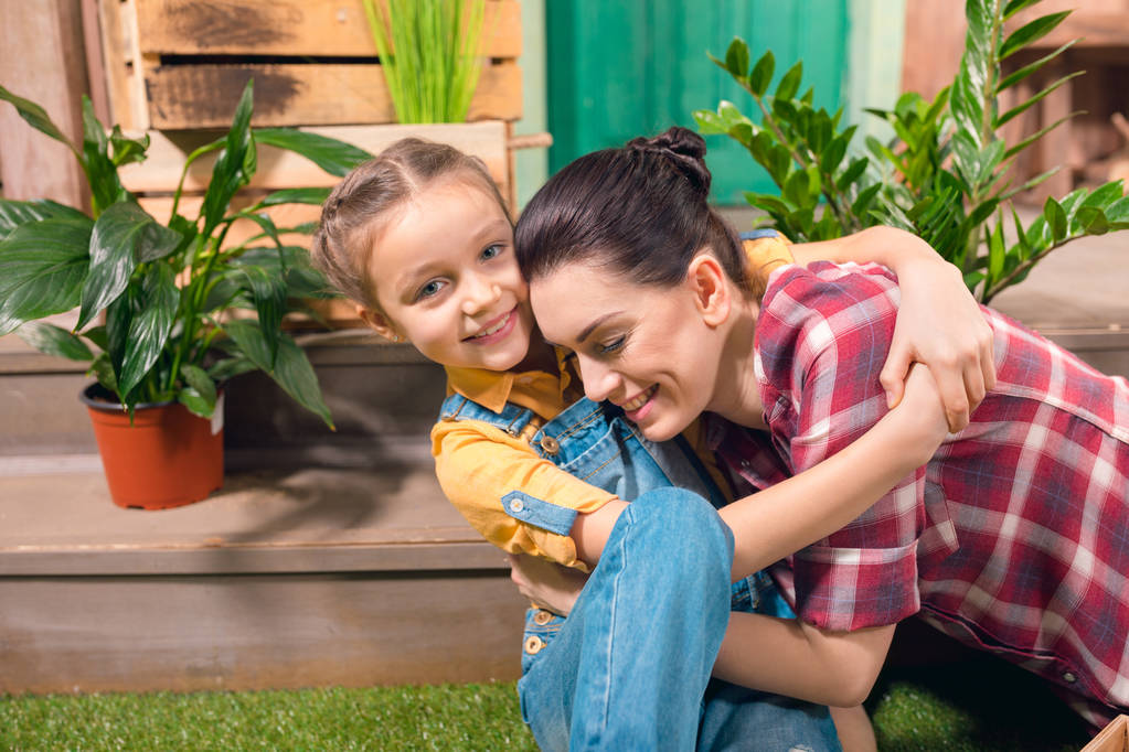 glückliche Mutter und Tochter umarmen sich auf Veranda mit Topfpflanzen  - Foto, Bild