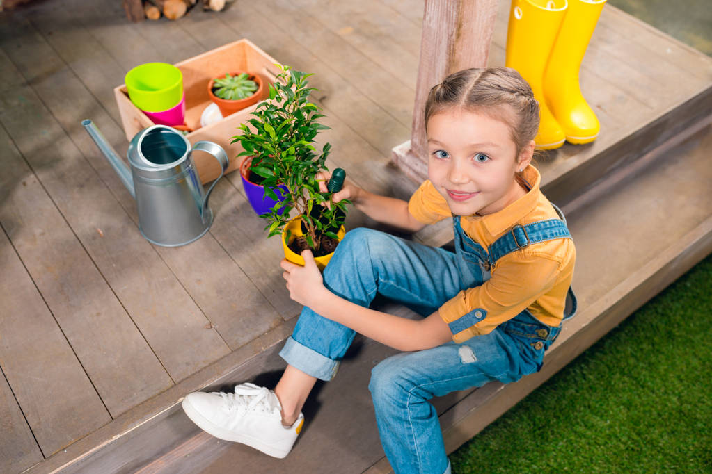 Vue grand angle de adorable petite fille assise sur le porche et cultivant la plante verte en pot
 - Photo, image