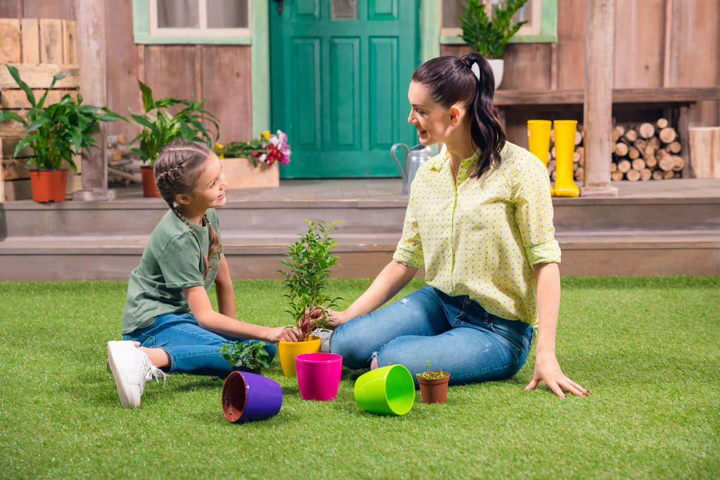 mère et fille avec des plantes et des pots de fleurs assis sur l'herbe verte
 - Photo, image