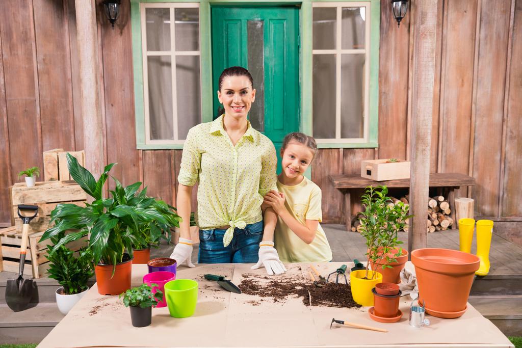 madre e hija con plantas y macetas de pie a la mesa en el porche
 - Foto, imagen