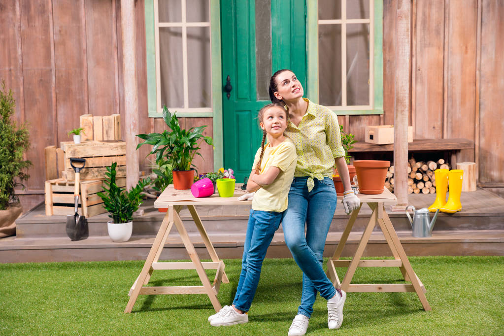 mãe e filha com plantas e vasos de flores de pé e abraçando à mesa na varanda
  - Foto, Imagem
