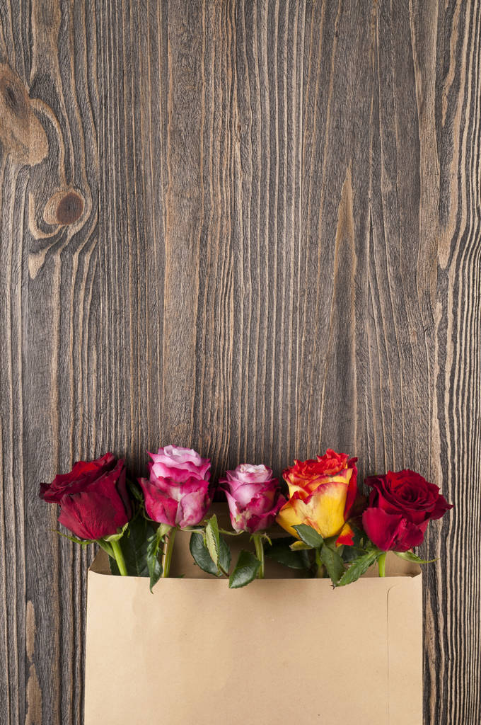 Μάτσο πολύχρωμα ροδαλά λουλούδια σε φάκελο χαρτί πάνω από τις ξύλινες β - Φωτογραφία, εικόνα
