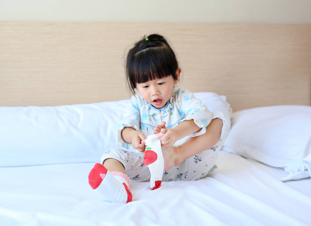 Чарівна маленька дівчинка намагається покласти шкарпетки на ліжко
. - Фото, зображення