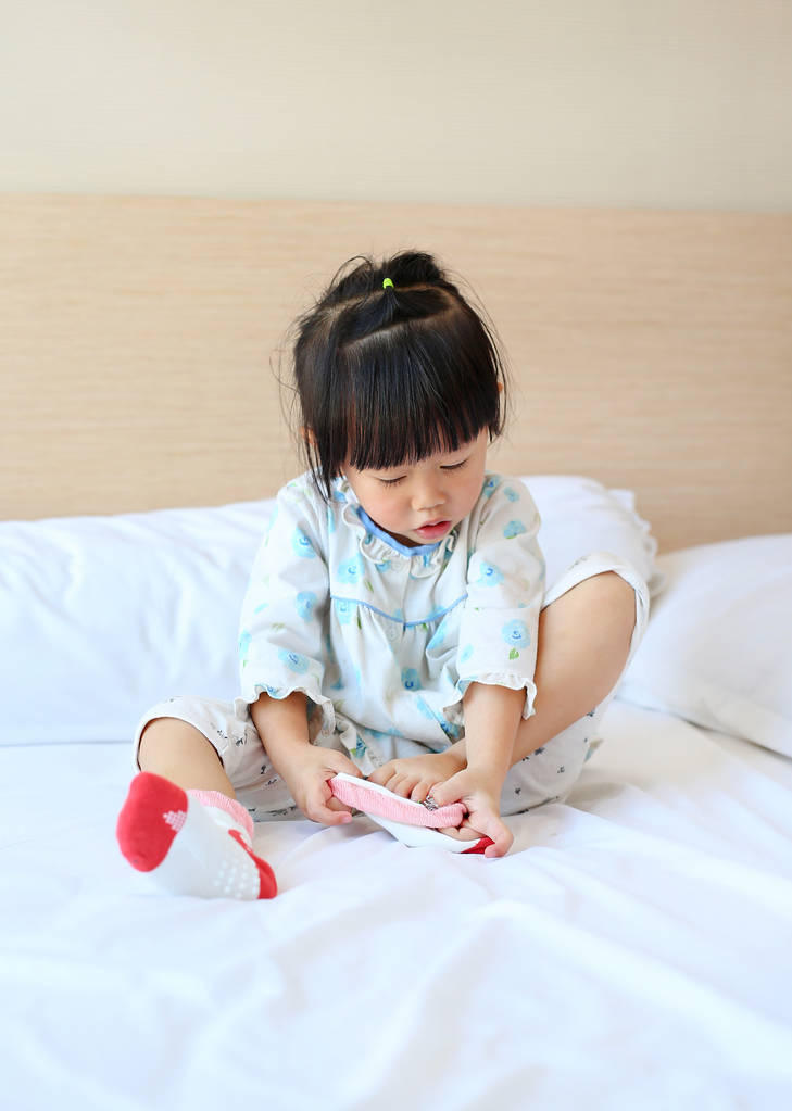 Aranyos kislány, kipróbálás-hoz tesz egy zoknit az ágyban. - Fotó, kép