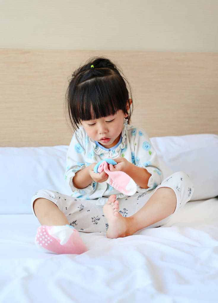 Adorable petite fille essayant de mettre une chaussette sur le lit
. - Photo, image