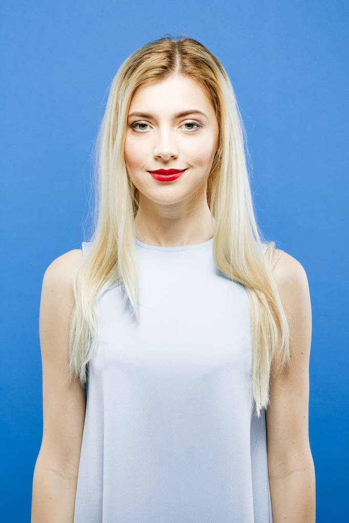 Portret atrakcyjna blondynka z długimi włosami, noszenie sukienka pozowanie na niebieskim tle w Studio. - Zdjęcie, obraz