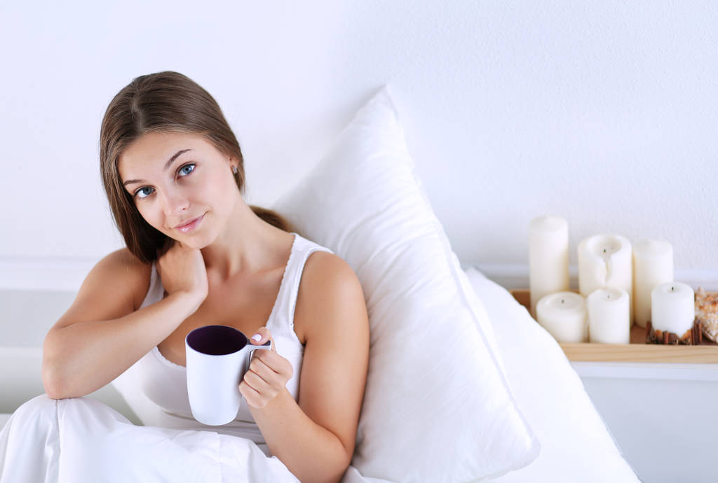 Jolie jeune femme au lit profitant d'une tasse de thé
 - Photo, image