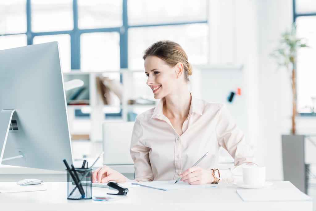 smiling businesswoman working on computer at office - Photo, Image