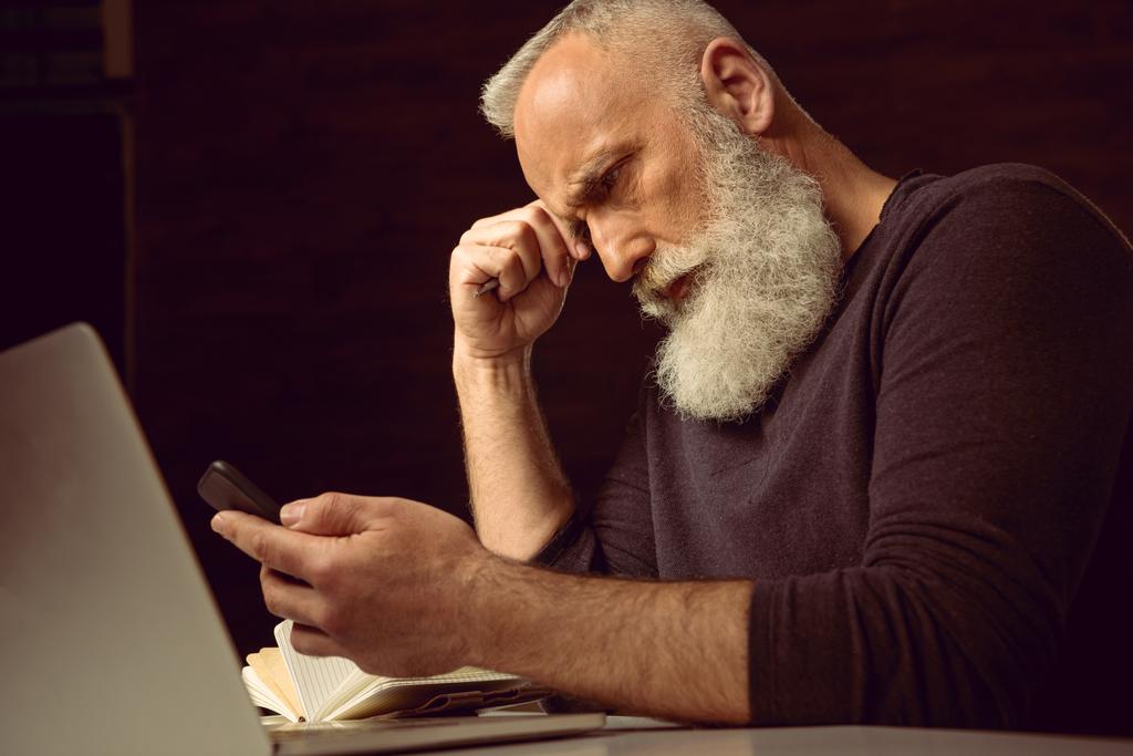 ο άνθρωπος που κάθεται στο τραπέζι και χρησιμοποιώντας το smartphone - Φωτογραφία, εικόνα