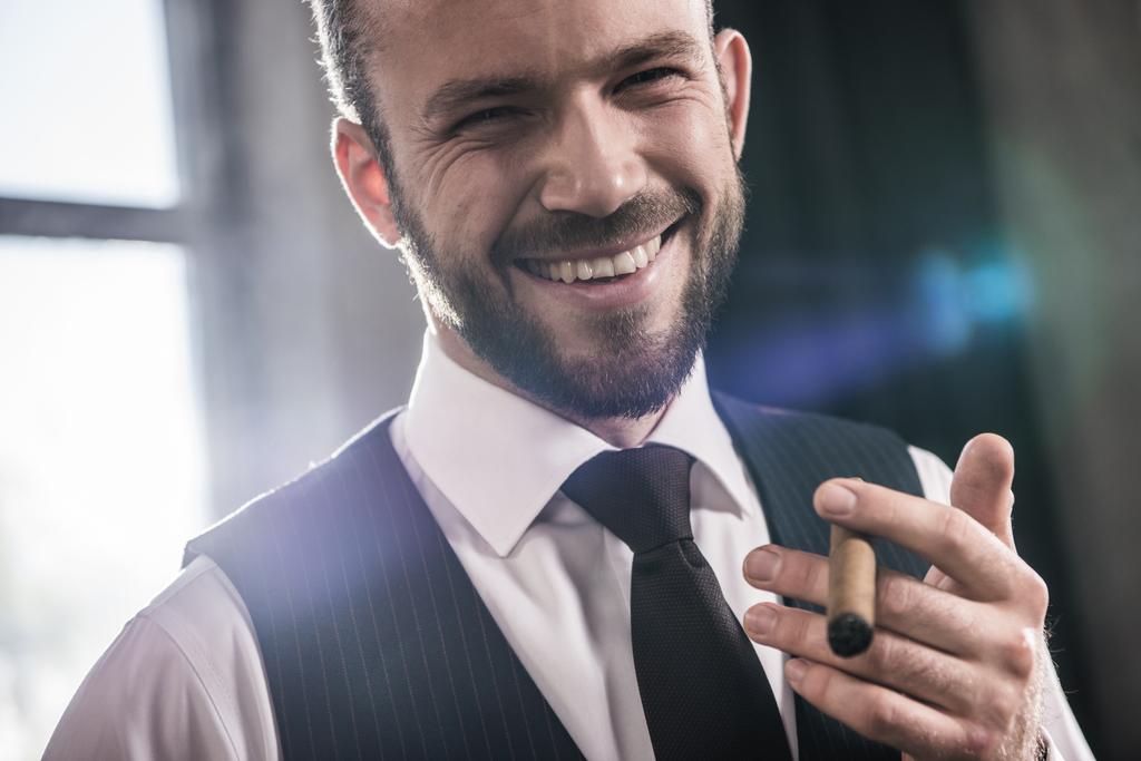 Primer plano retrato de guapo sonriente confiado hombre fumando cigarro en el interior
   - Foto, imagen