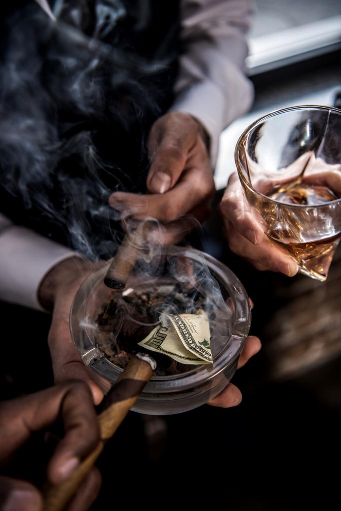 Γκρο πλαν μερική άποψη των επιχειρηματιών με τραπεζογραμμάτιο δολάριο σε τασάκι πίνοντας ουίσκι και καπνίζοντας πούρα - Φωτογραφία, εικόνα