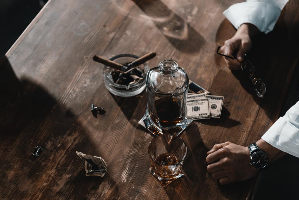 dollar bankbiljetten, whisky en sigaren in de asbak op houten tafel - Foto, afbeelding