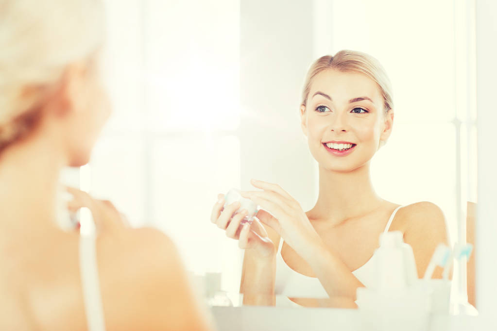 onnellinen nainen soveltamalla kerma kasvotusten kylpyhuoneessa
 - Valokuva, kuva