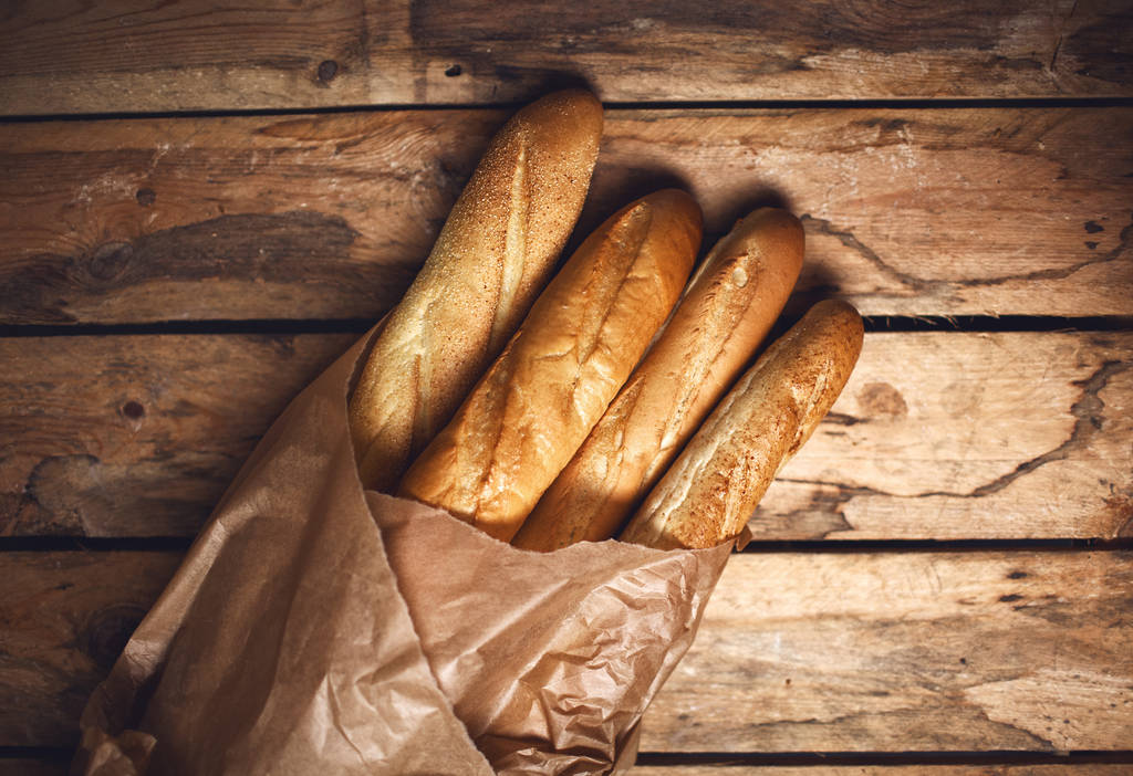 čtyři bochníky chleba bageta v papírový sáček na dřevěné pozadí - Fotografie, Obrázek