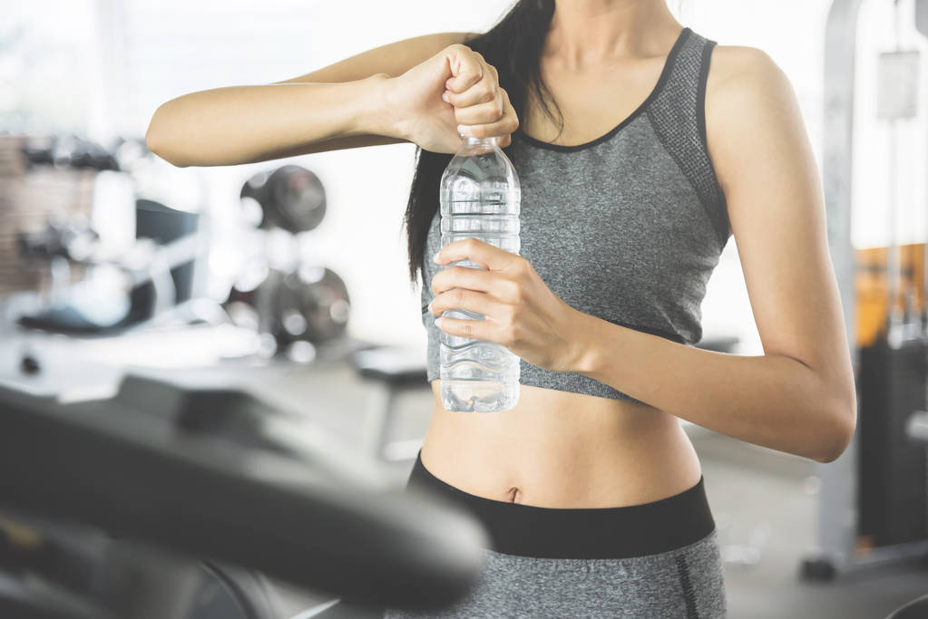 Азиатка в спортивной одежде держит бутылку воды в спортзале
. - Фото, изображение