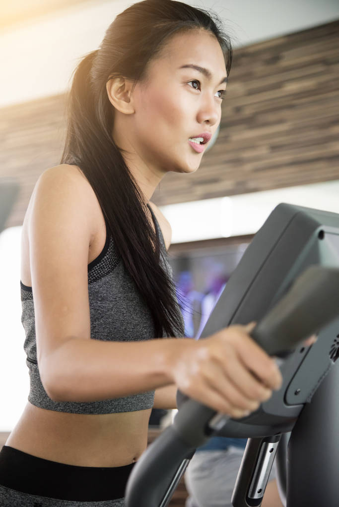 Asyalı kadın spor salonunda eliptik eğitmen makinede egzersiz. - Fotoğraf, Görsel