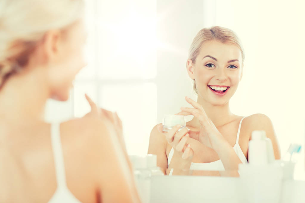 Szczęśliwa kobieta nałożeniem kremu do twarzy w łazience - Zdjęcie, obraz