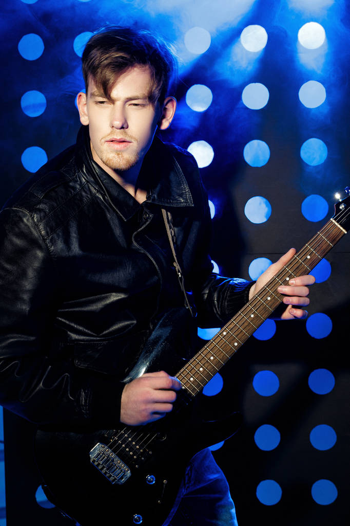 mladá atraktivní rockový hudebník hraje na elektrickou kytaru a zpívá. Rocková hvězda na pozadí reflektorů - Fotografie, Obrázek