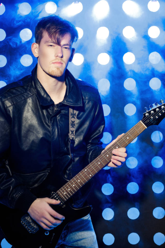 jonge aantrekkelijke rockmuzikant elektrische gitaar spelen en zingen. Rockster op achtergrond van spots - Foto, afbeelding