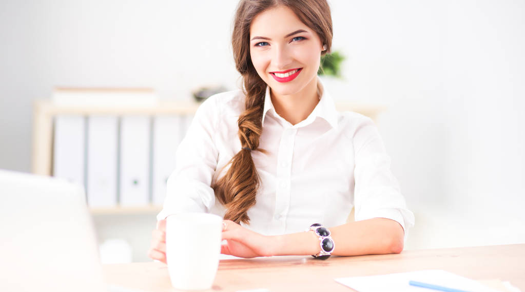 Junge Geschäftsfrau sitzt mit Tasse im Büro auf dem Schreibtisch - Foto, Bild