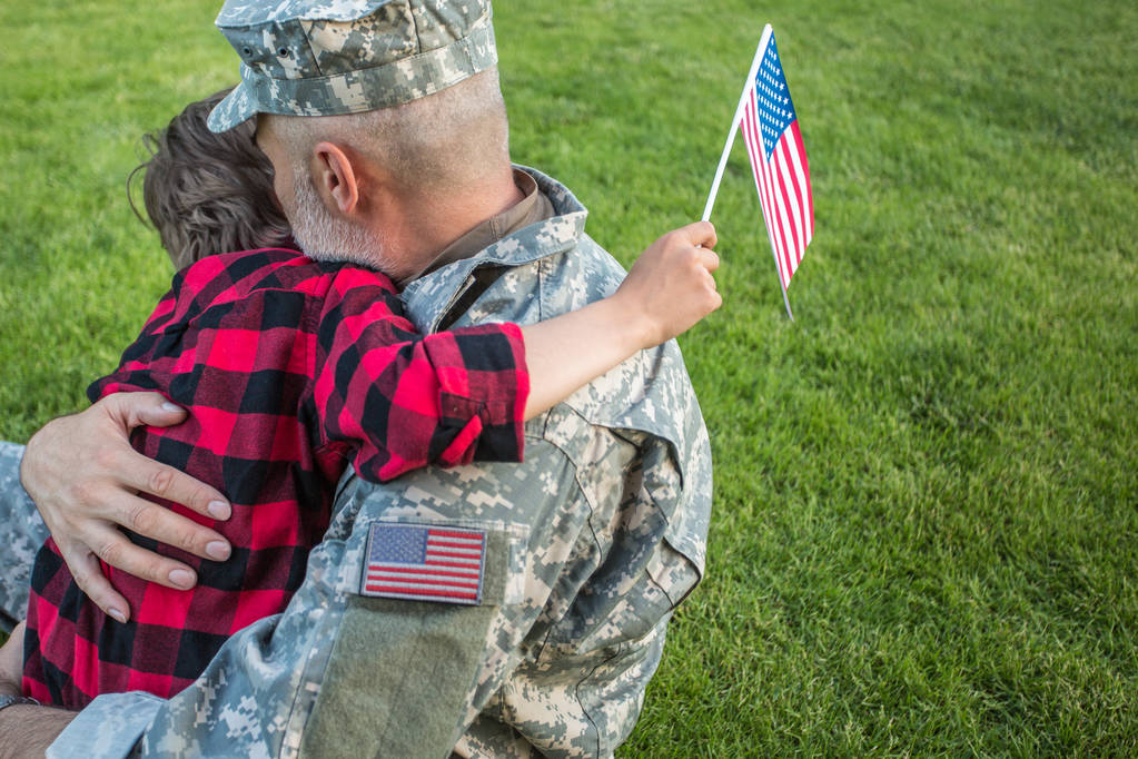 Amerykański żołnierz zjednoczona z synem siedząc na zielonej trawie - Zdjęcie, obraz