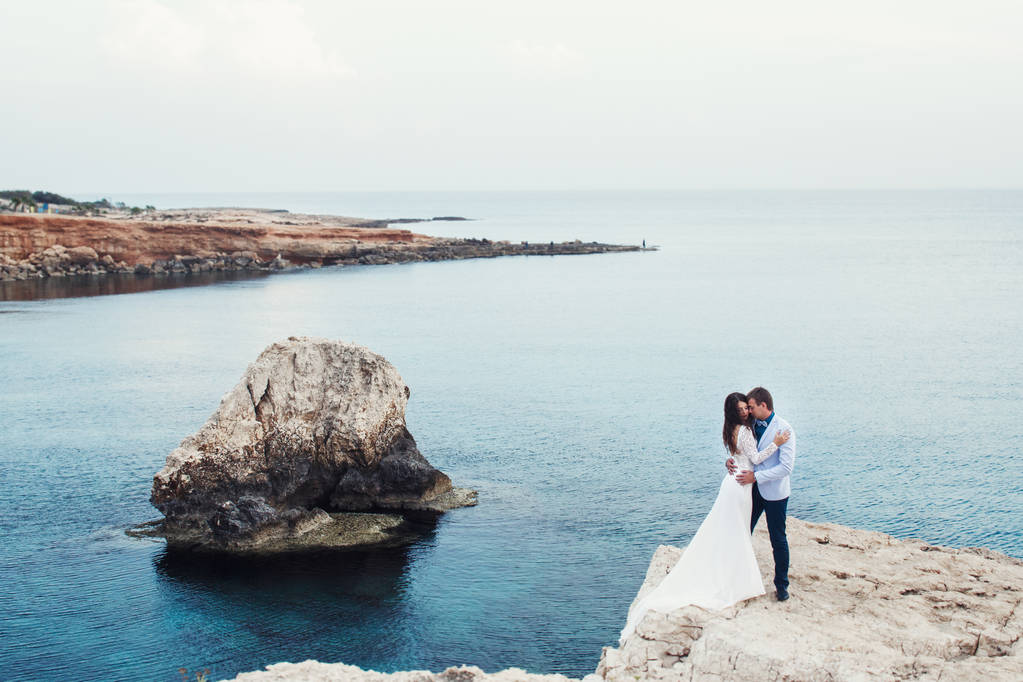 Hugging couple stands on the rock over the azure sea  - Photo, Image