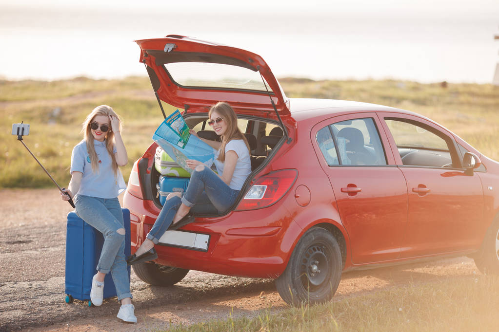 Twee mooie vrouwen zijn reizen op een rode auto - Foto, afbeelding