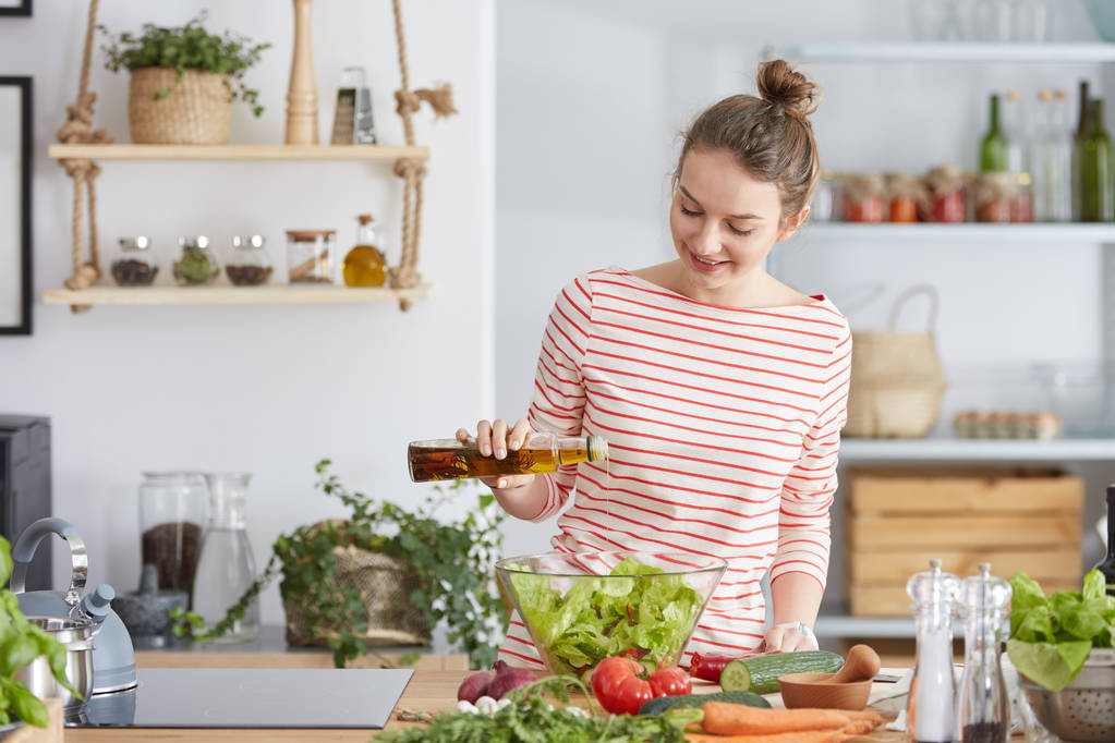 Vrouw olijfolie toe te voegen aan een salade - Foto, afbeelding