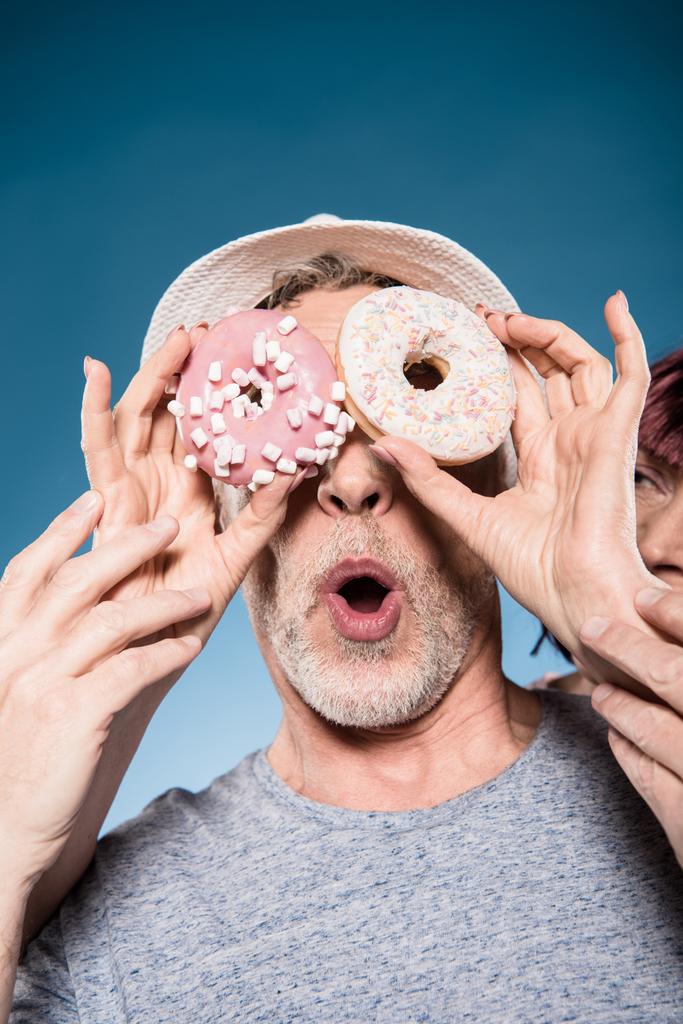 elderly couple fooling around with doughnuts - Photo, Image