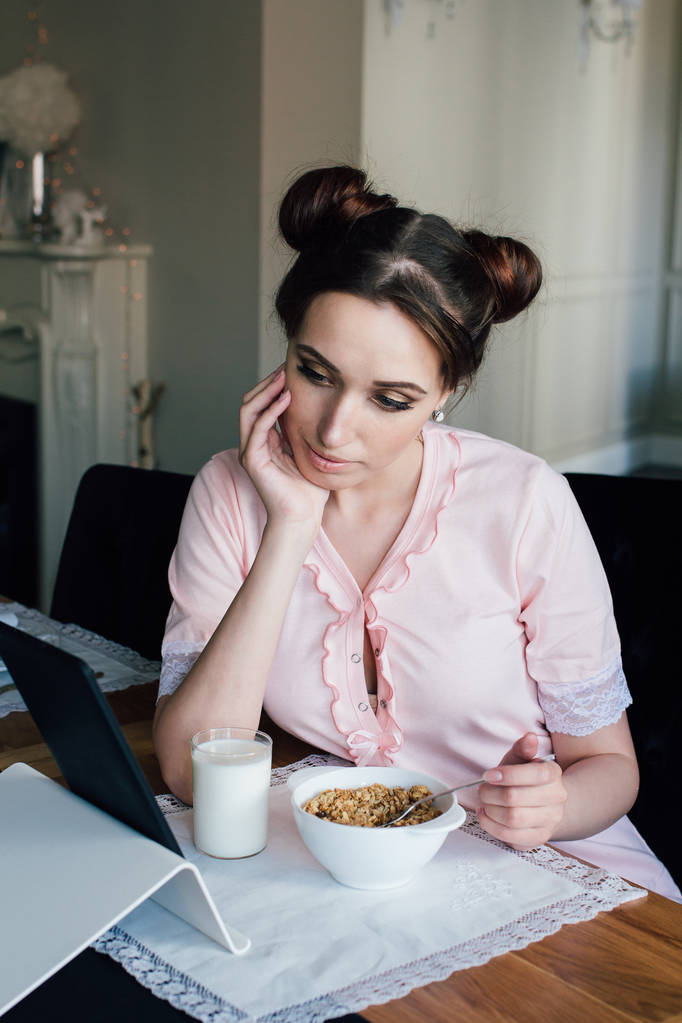Woman having Breakfast with cereals and milk and looks at tablet - Photo, Image