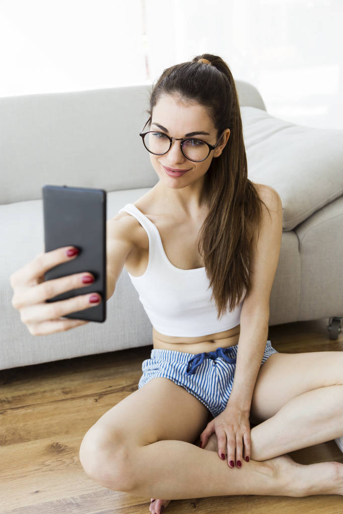 Красива молода жінка використовує свій мобільний телефон вдома
. - Фото, зображення
